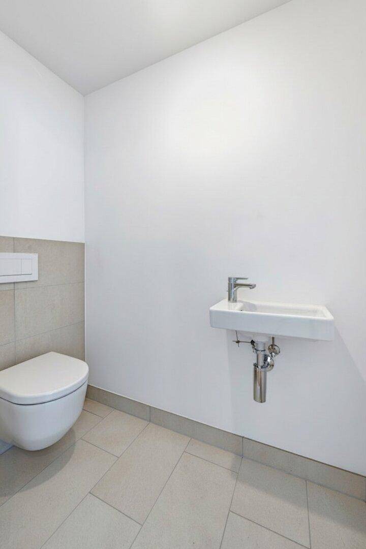 Kleines Gäste-WC mit wandhängender Toilette und kompaktem Waschbecken, hell gefliest.