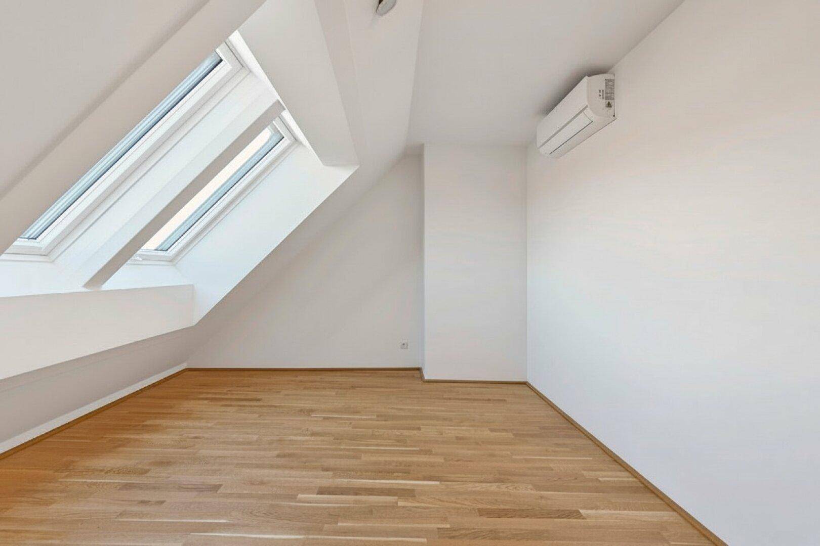 Heller Dachgeschossraum mit Holzboden, Dachfenstern und Klimaanlage, ideal für flexible Nutzung.
