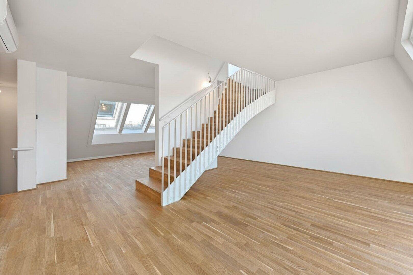 Geräumiger Wohnbereich im Dachgeschoss mit eleganter Holztreppe und hellem Parkettboden.