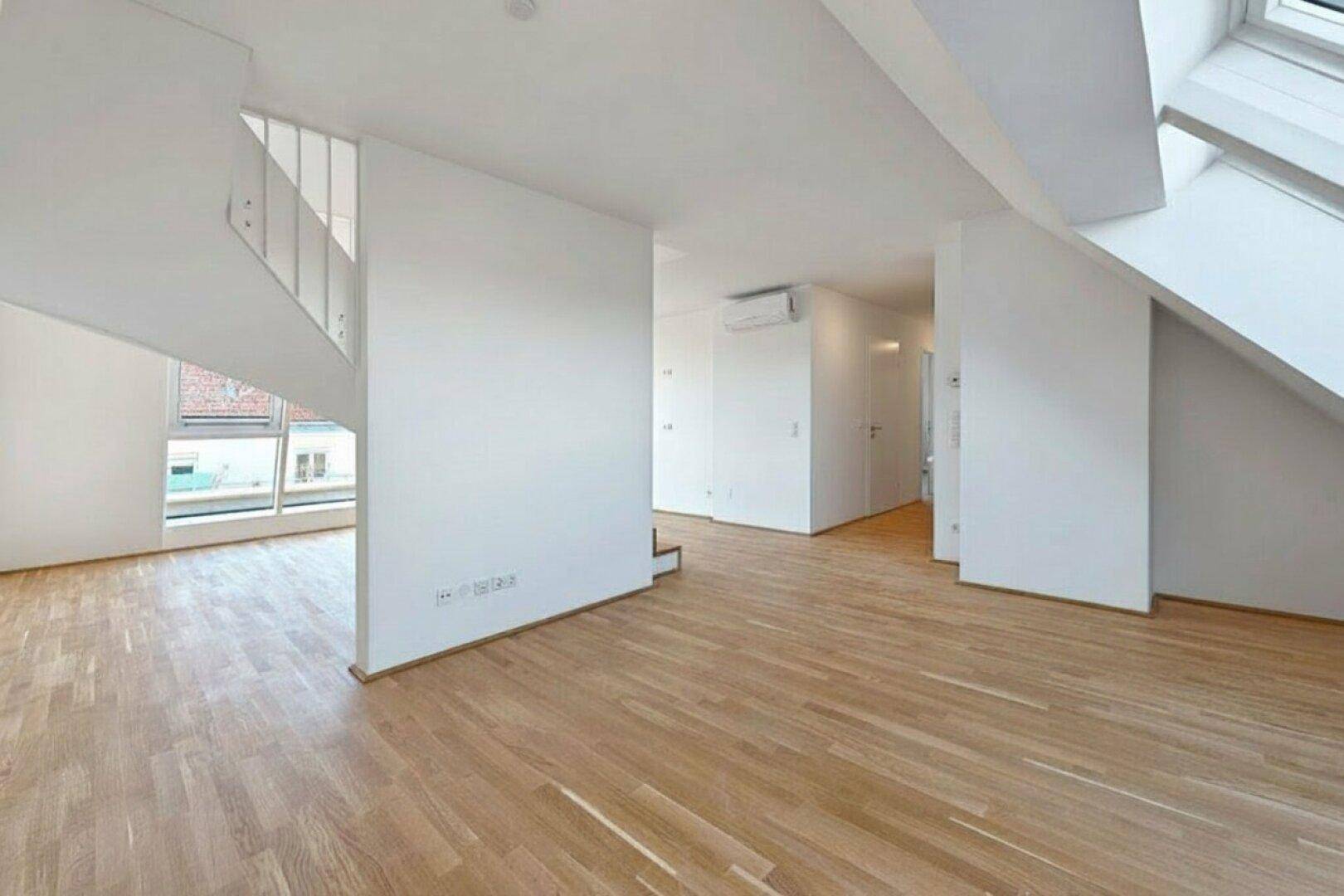 Offener Wohnbereich mit Holztreppe, großen Fenstern und hellem Parkettboden im Dachgeschoss.