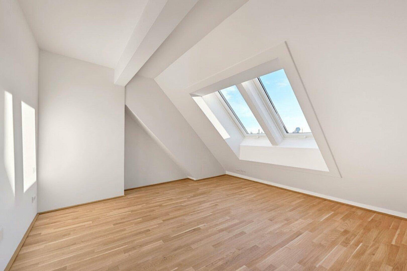 Dachgeschossraum mit schrägen Wänden, Holzboden und mehreren Dachfenstern für viel Tageslicht.