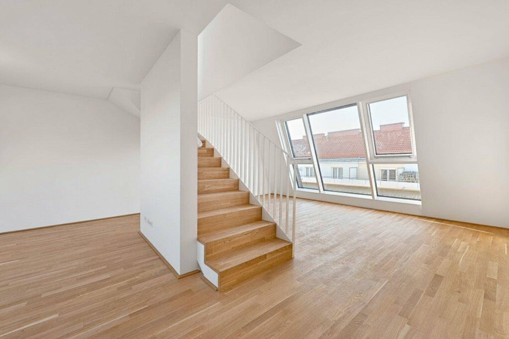 Offener Wohnbereich im Dachgeschoss mit Holztreppe, großen Fenstern und weitem Stadtblick.