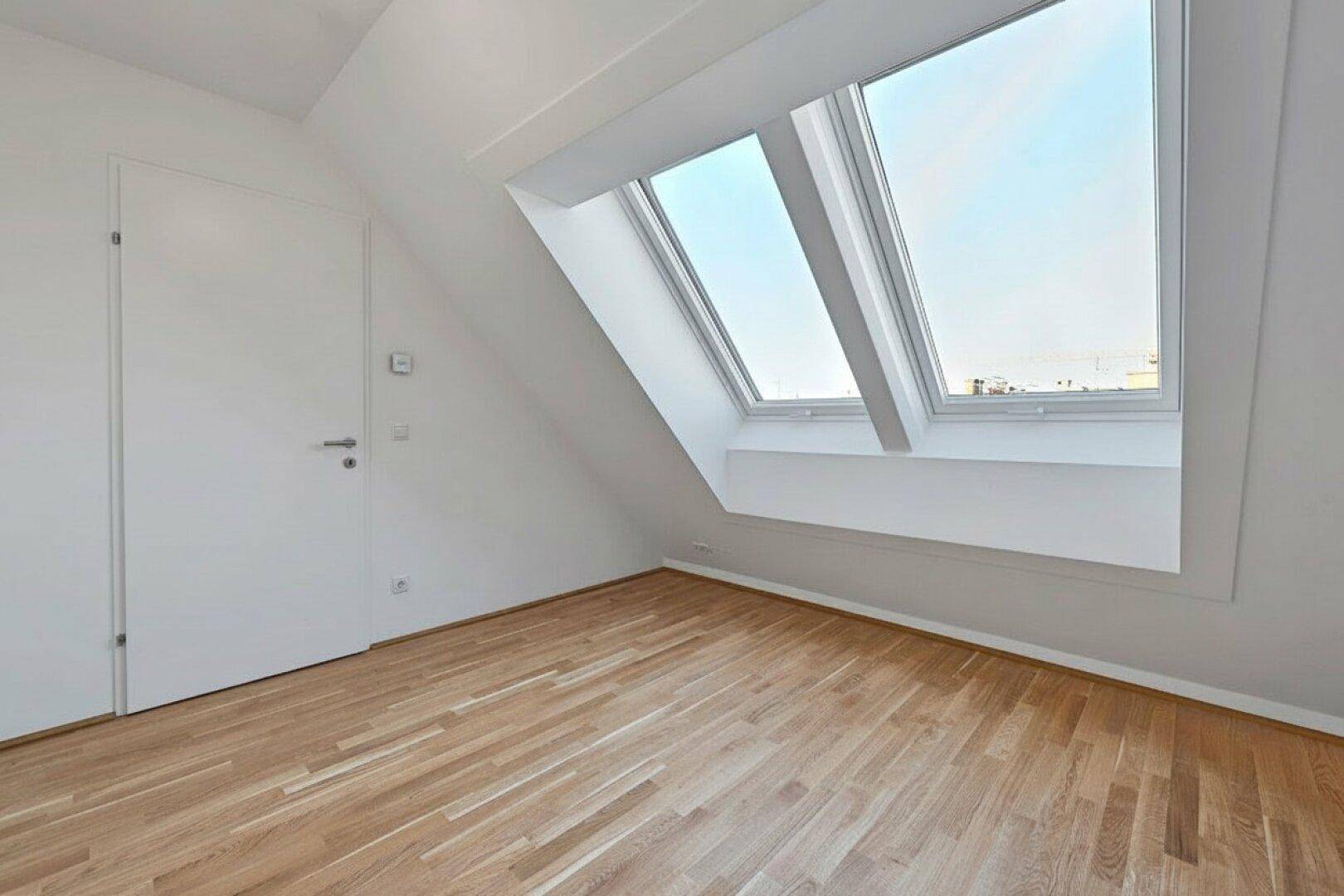 Dachgeschossraum mit Holzboden, einer Tür und großem Dachfenster für optimale Belichtung.