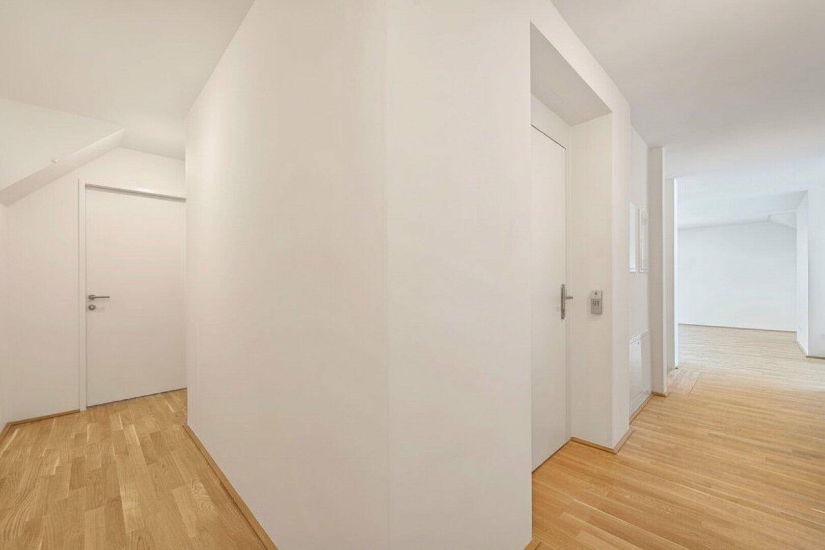 Heller Flur im Dachgeschoss mit Holzboden und weißen Wänden, der verschiedene Räume verbindet.
