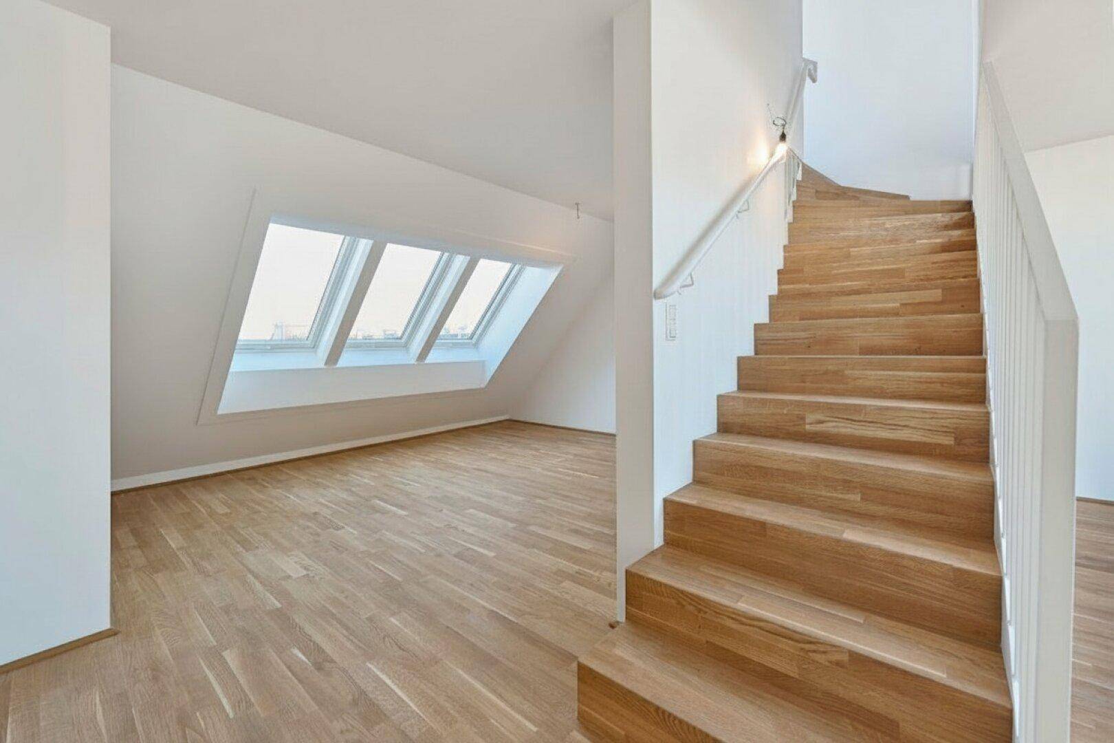 Offener Wohnbereich mit Holztreppe, Parkettboden und Dachfenstern, die viel Licht hereinlassen.