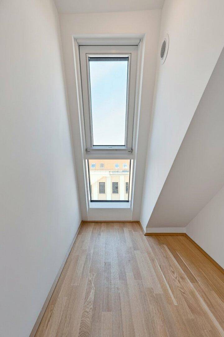 Schmaler Raum im Dachgeschoss mit Holzboden und hohem Dachfenster, ideal als Abstellraum oder Nische.