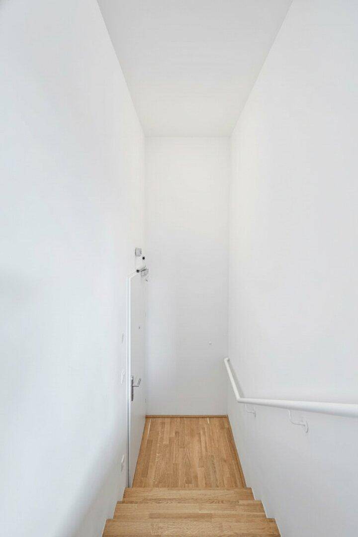 Heller Treppenaufgang mit Holzstufen und weißem Geländer, der die Etagen verbindet.