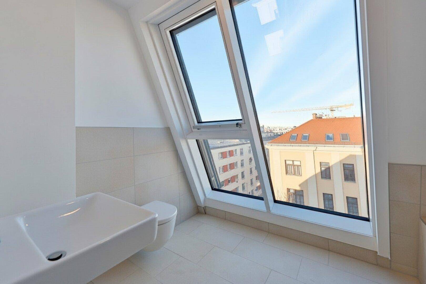 Helles Badezimmer mit Waschbecken, Toilette und großem Dachfenster mit Stadtblick.