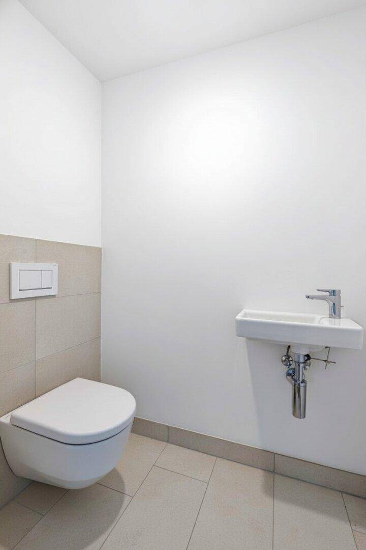 Modernes Gäste-WC mit wandhängender Toilette und kleinem Waschbecken, in hellen Farben gehalten.