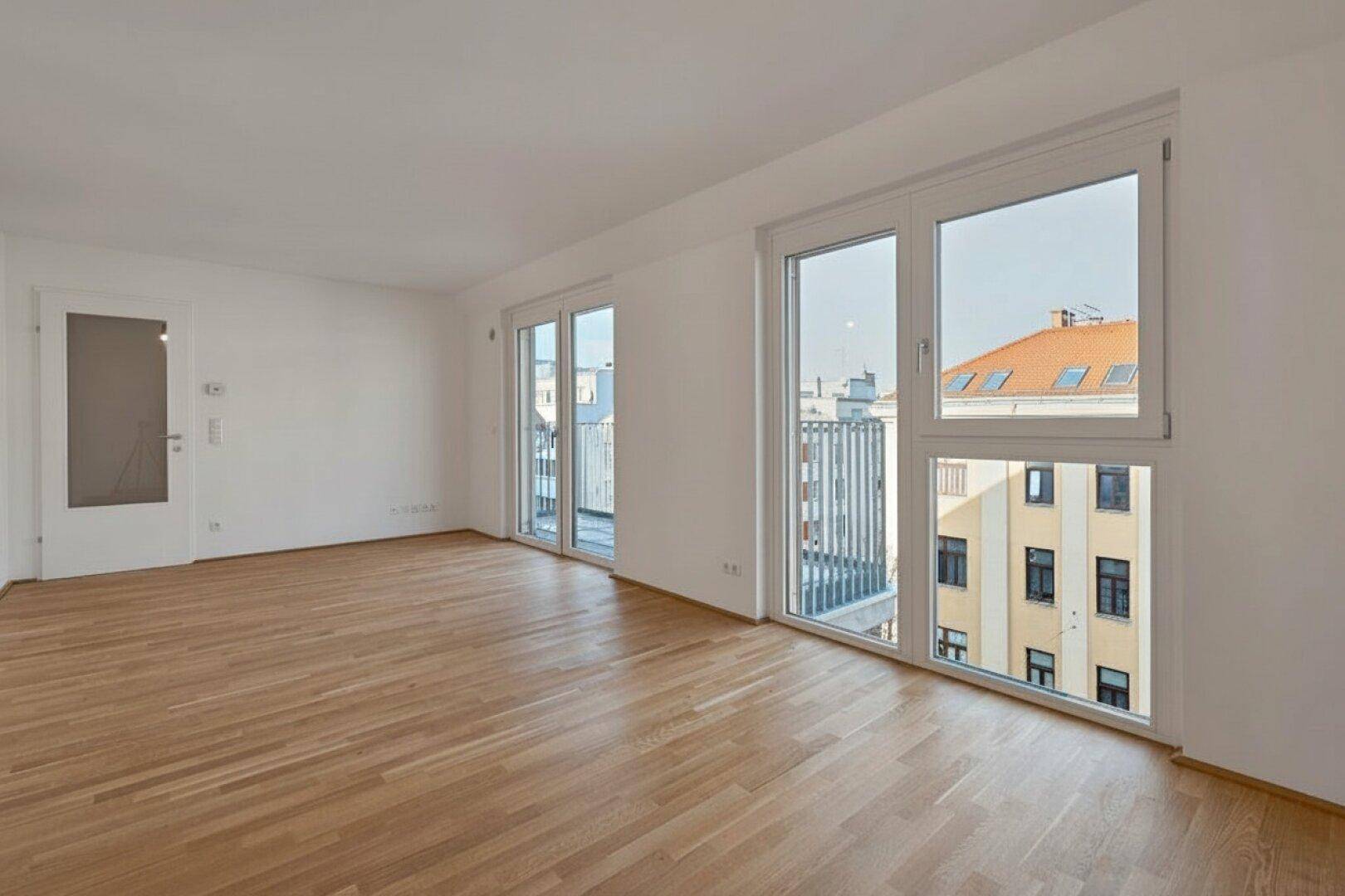 Helles Wohnzimmer mit Parkettboden, großen Fenstern und Zugang zu einem französischen Balkon.