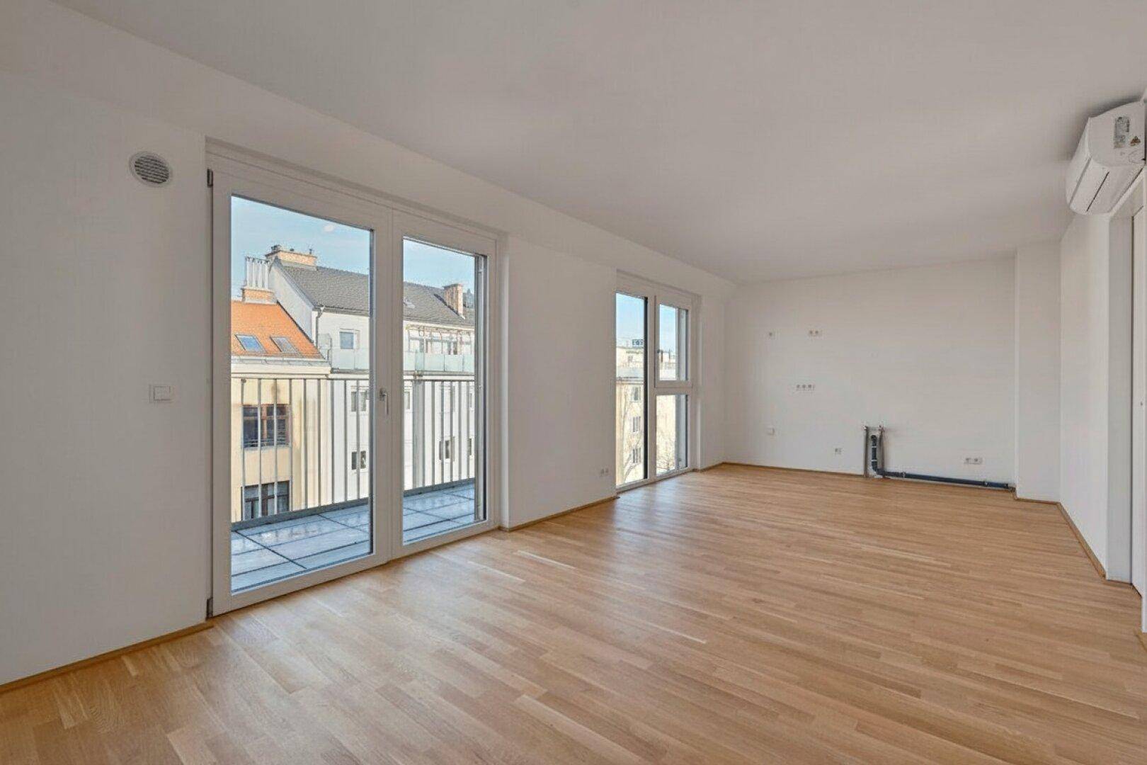 Geräumiger Wohnbereich mit Parkettboden, Klimaanlage und Zugang zu einem Balkon mit Geländer.
