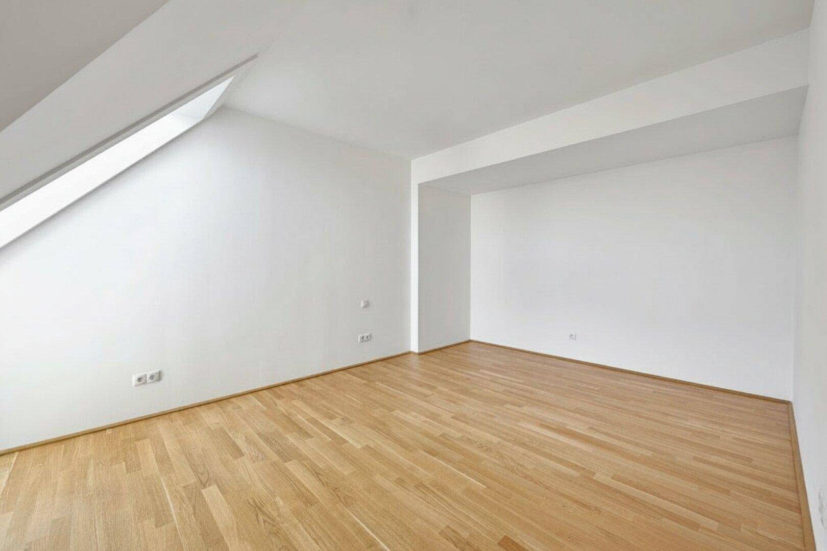 Leeres Zimmer im Dachgeschoss mit Parkettboden und Dachschräge, bereit zur individuellen Gestaltung.