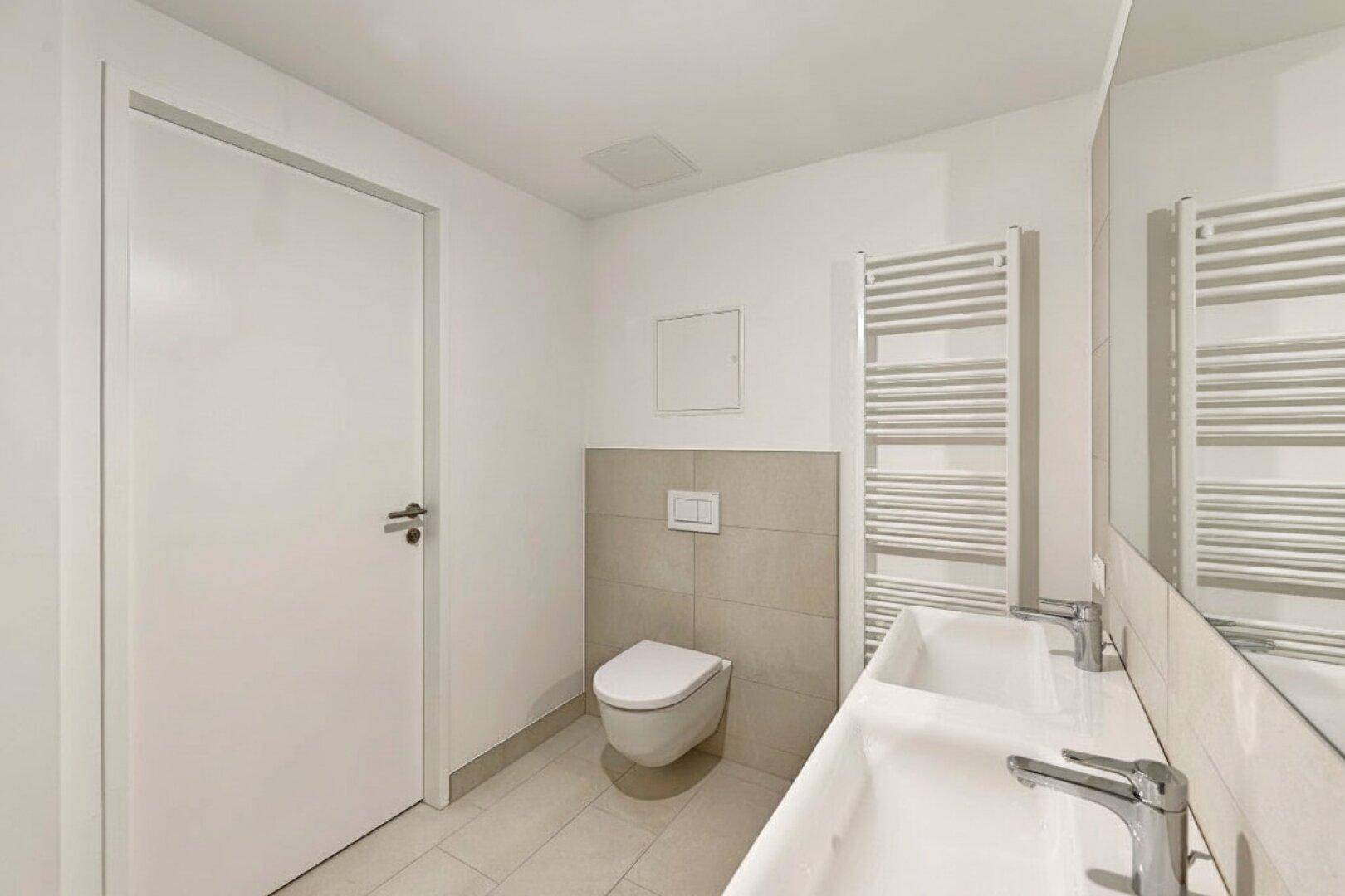 Modernes Badezimmer mit Doppelwaschbecken, Wand-WC und beheiztem Handtuchhalter.