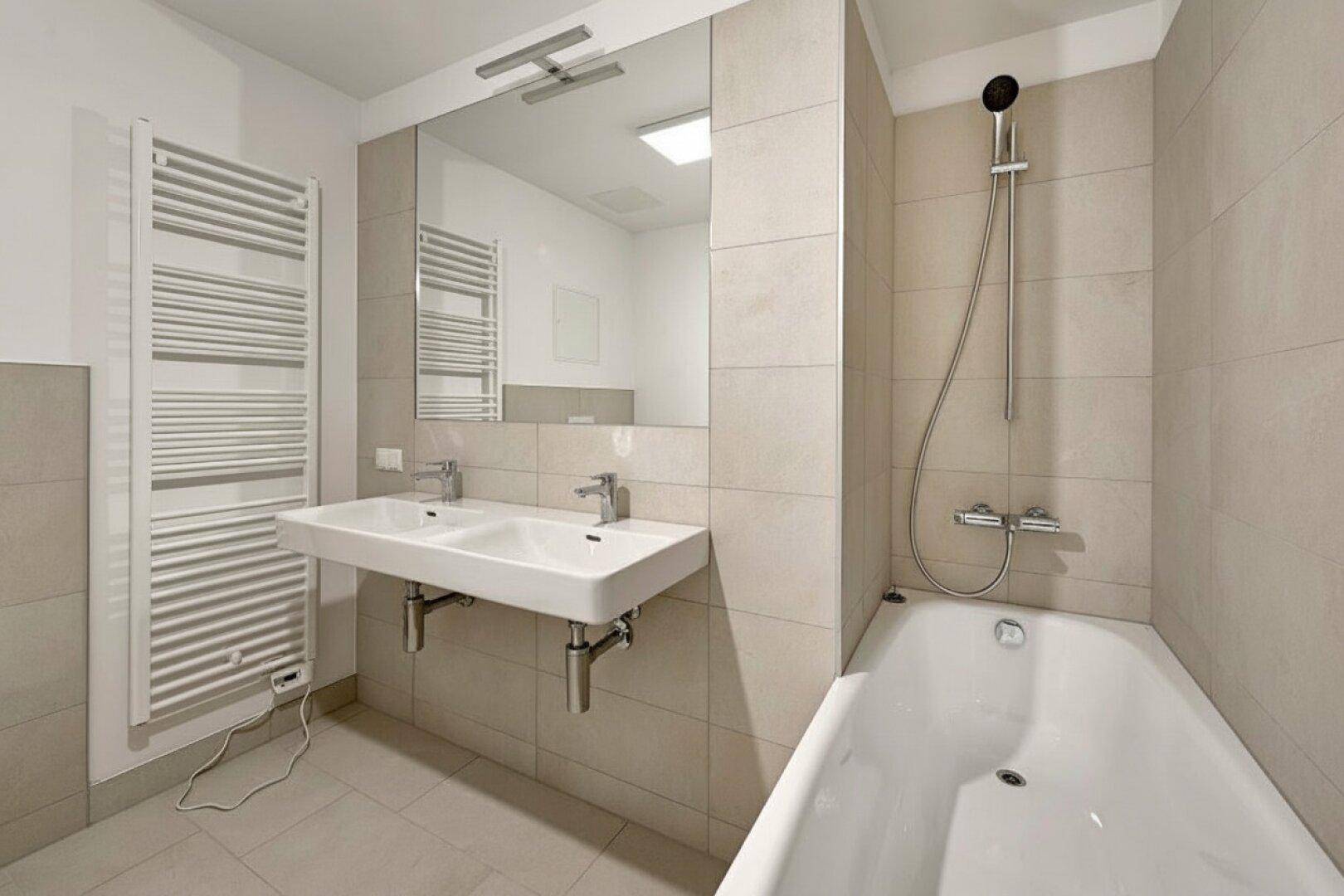 Helles Badezimmer mit Badewanne, Doppelwaschbecken und großem Spiegel, modern gefliest.