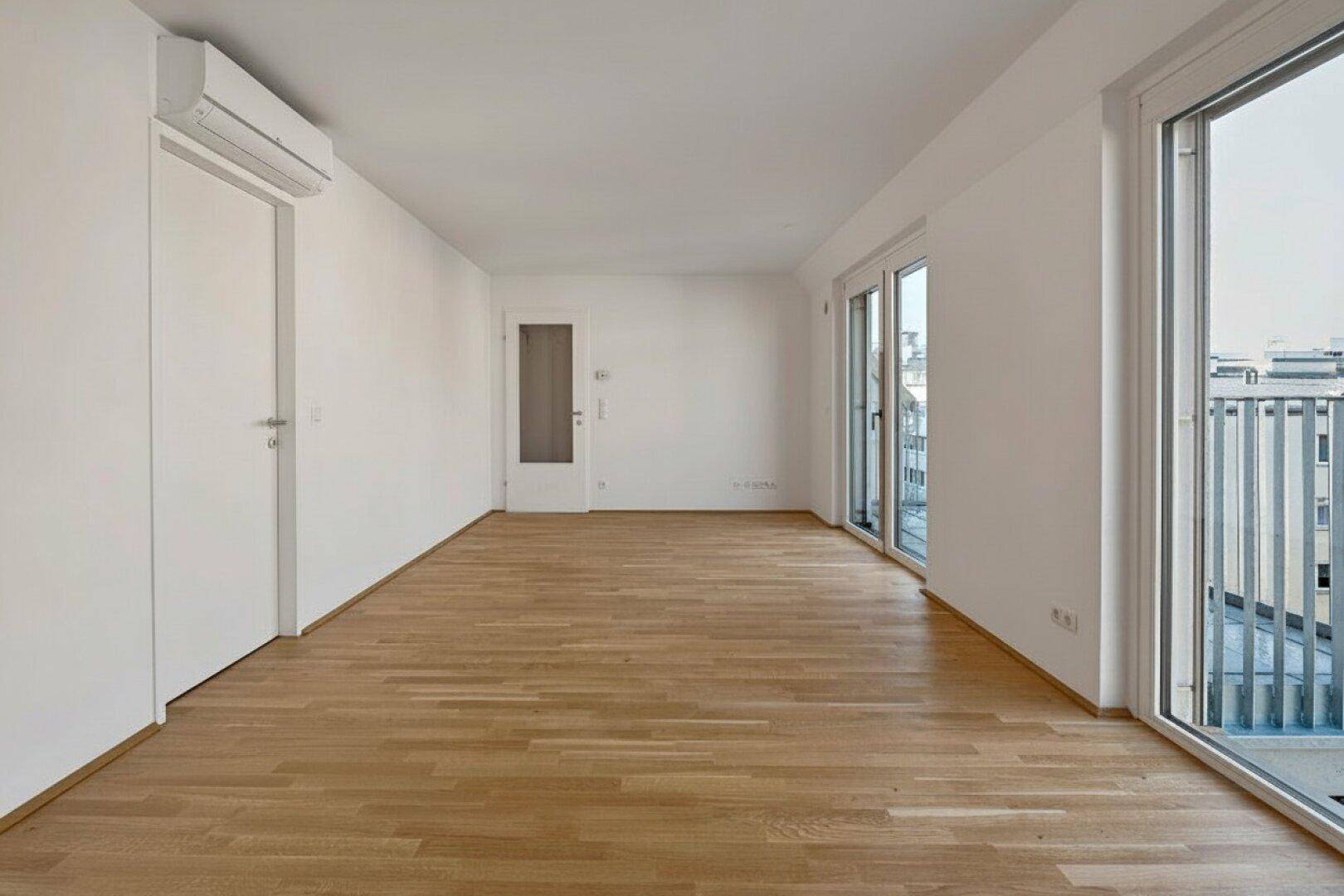 Langer, heller Wohnraum mit Parkettboden, Klimaanlage und großen Fenstern mit Balkonzugang.