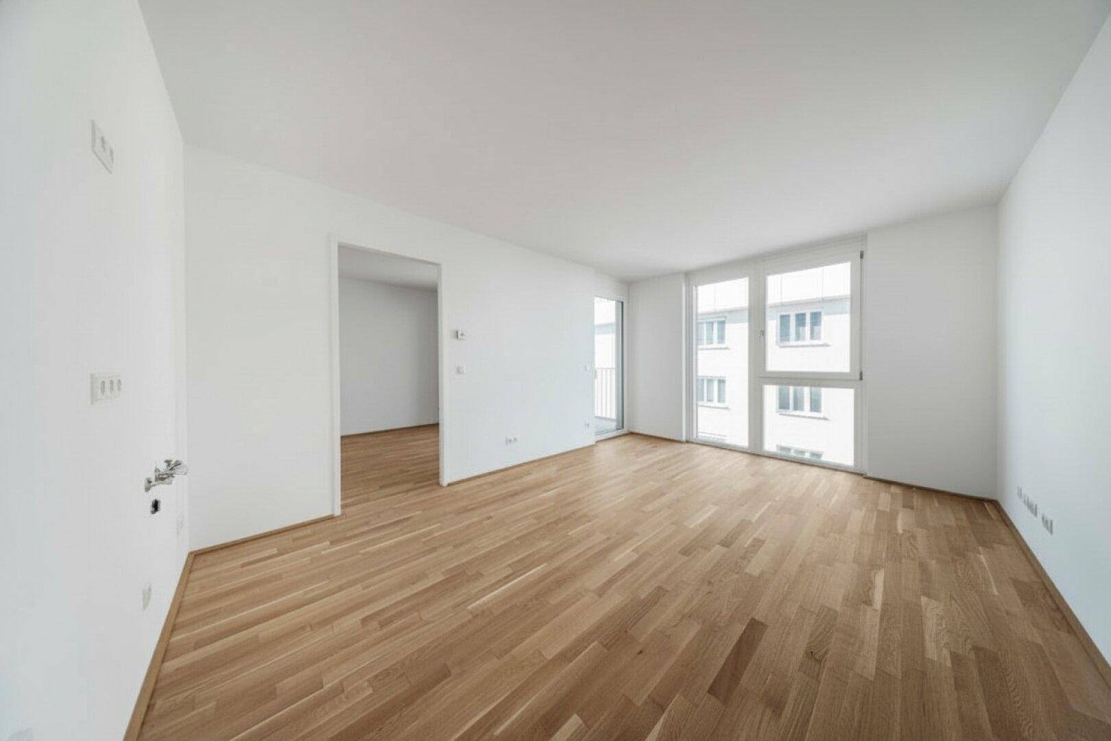 Heller Raum mit Parkettboden und Zugang zu weiteren Zimmern sowie großen Fenstern.