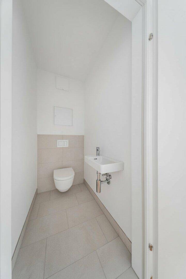 Modernes Gäste-WC mit Wand-WC und kleinem Waschbecken, hell gefliest.