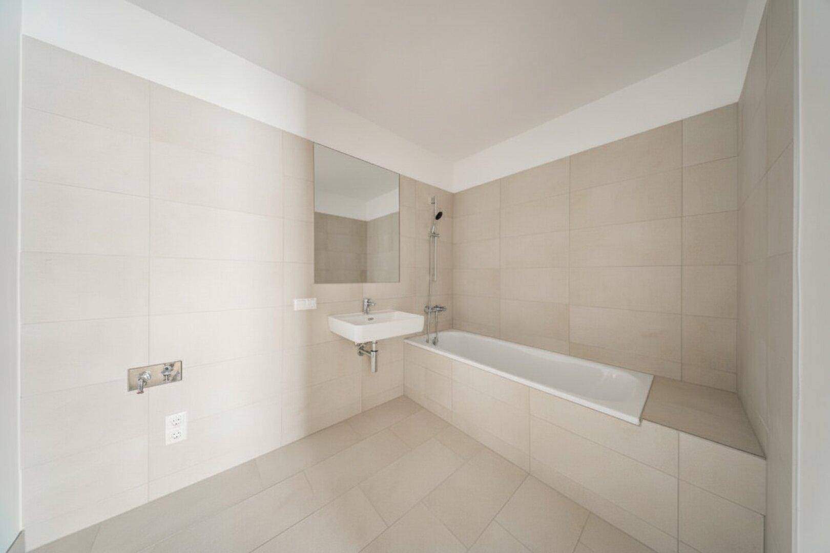 Modernes Badezimmer mit Badewanne und Waschbecken, komplett gefliest in neutralen Farben.