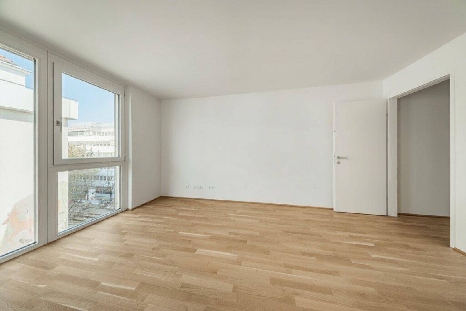 Geräumiger, leerer Raum mit großen Fenstern und hellem Parkettboden, ideal für vielseitige Nutzung.
