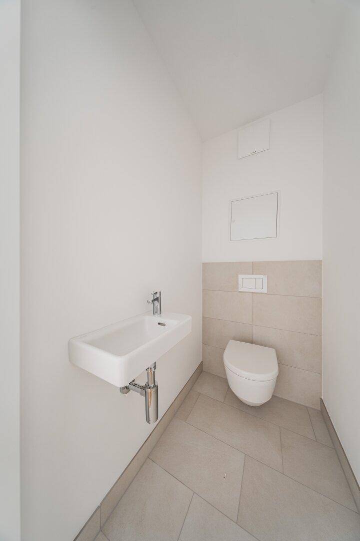 Funktionale Gästetoilette mit wandhängendem WC und kleinem Handwaschbecken, modern gefliest.