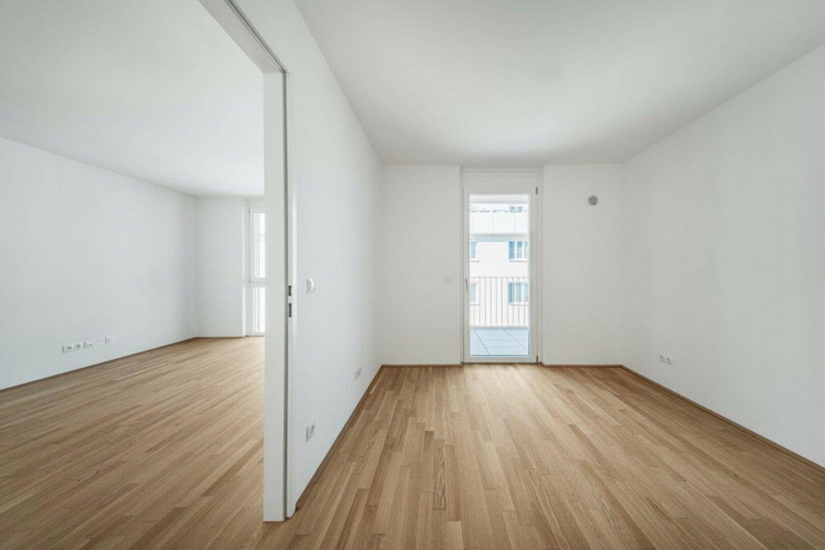 Helles Zimmer mit Holzboden und Balkontür, bietet eine ruhige Atmosphäre und Zugang ins Freie.