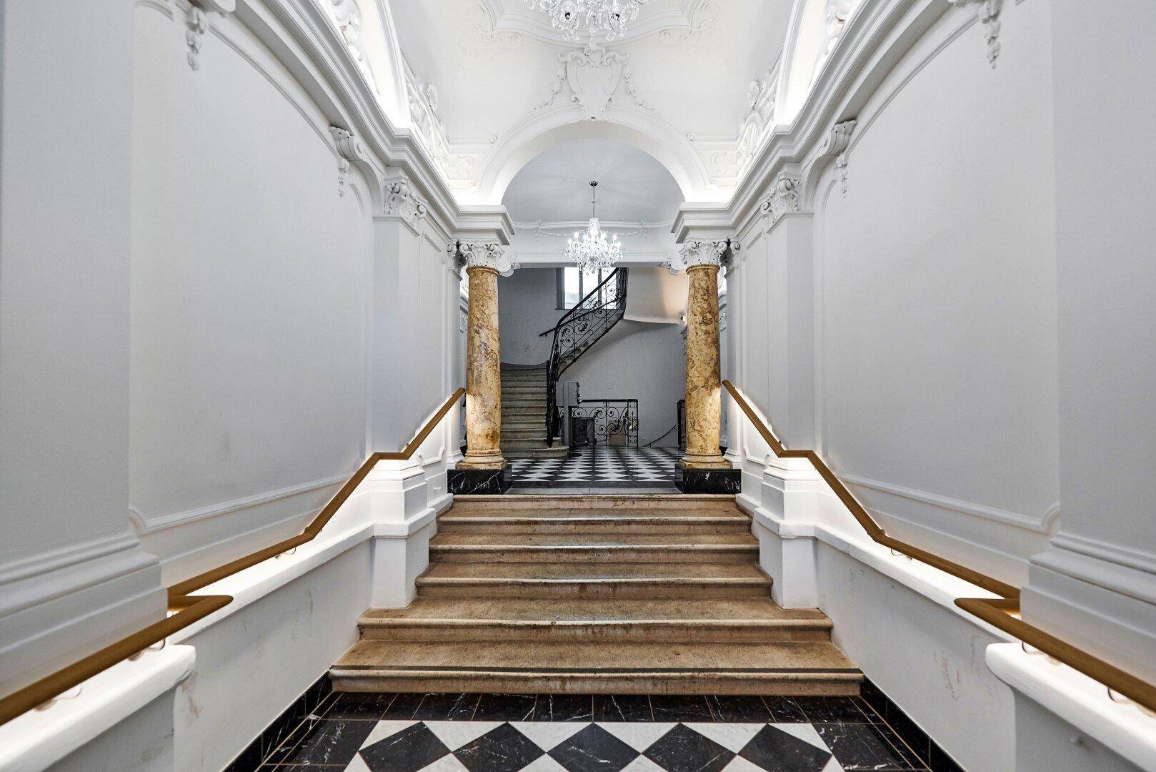 Elegante Eingangshalle mit Marmorsäulen, kunstvollem Stuck und Blick auf ein prunkvolles Treppenhaus.