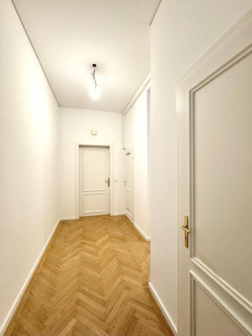 Langer, heller Flur mit Fischgrätparkett und mehreren weißen Türen, die zu den verschiedenen Zimmern führen.