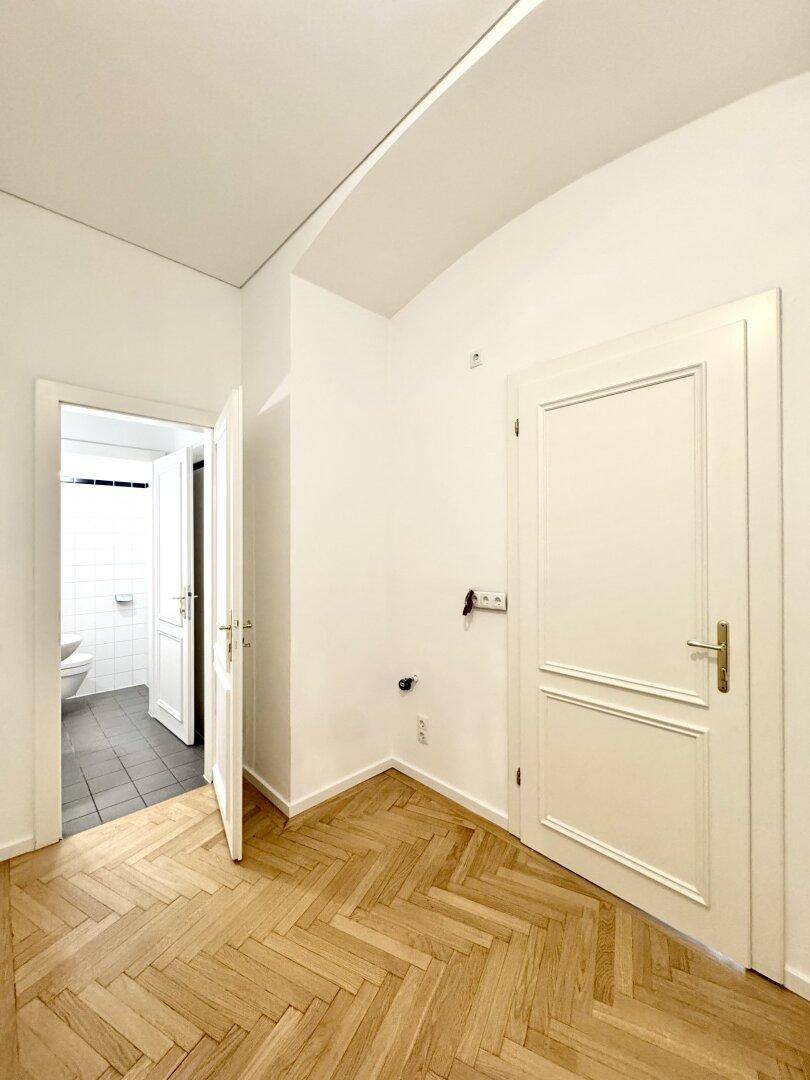 Heller Flurbereich mit Fischgrätparkett und Zugang zu einem Badezimmer, das durch eine offene Tür sichtbar ist.