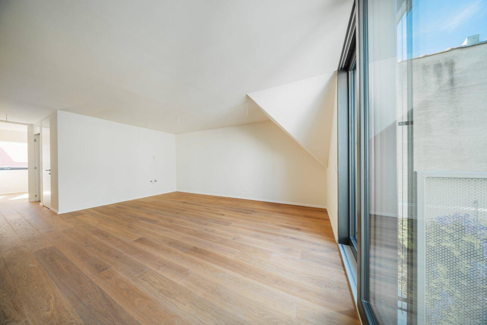 Heller Wohnraum mit Holzboden und großen Fenstern, die viel Tageslicht hereinlassen und einen offenen Übergang bieten.