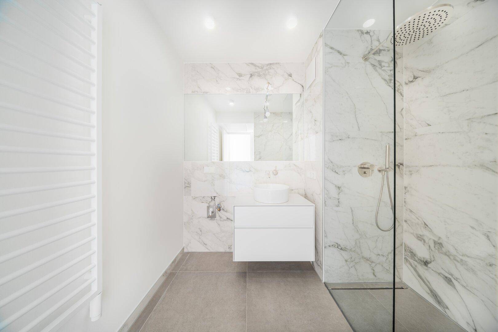 Modernes Badezimmer mit Marmorfliesen, begehbarer Dusche, Regenbrause und beheiztem Handtuchhalter.
