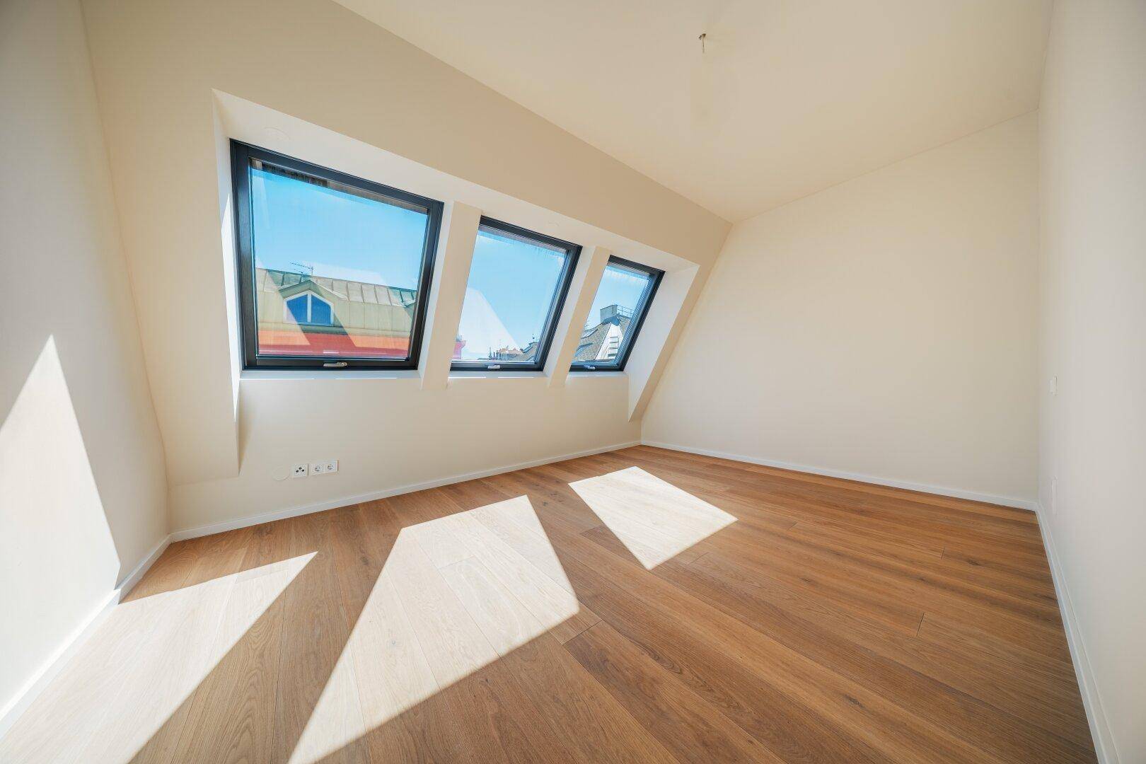 Helles Schlafzimmer mit Holzboden und drei Dachfenstern, die viel Sonnenlicht in den Raum lassen.