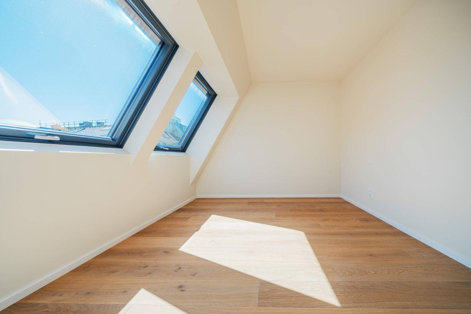 Lichtdurchflutetes Zimmer mit Parkettboden und zwei großen Dachfenstern, die den Raum erhellen.