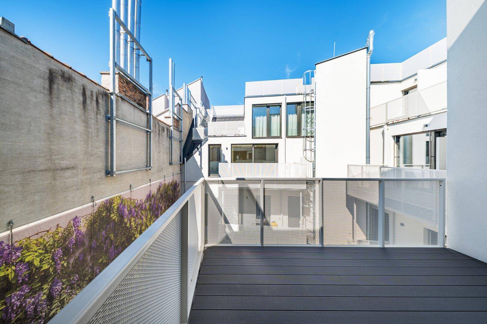 Geräumige Terrasse mit modernem Bodenbelag und Blick auf umliegende Gebäude sowie eine begrünte Wand.