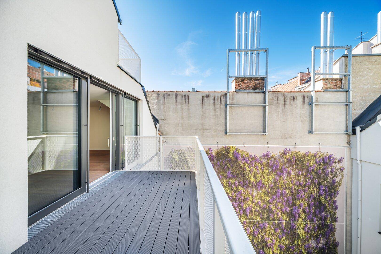 Moderne Terrasse mit Zugang vom Innenbereich und Blick auf die umliegende Architektur und eine Pflanzenwand.