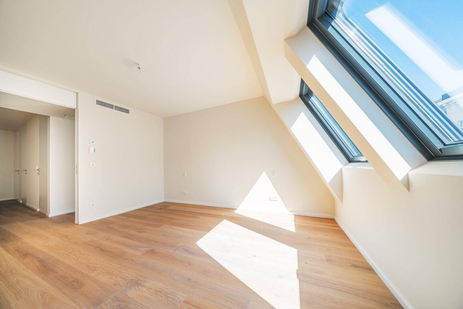 Heller Raum mit Holzboden und großem Dachfenster, das viel Sonnenlicht in den Raum lässt.