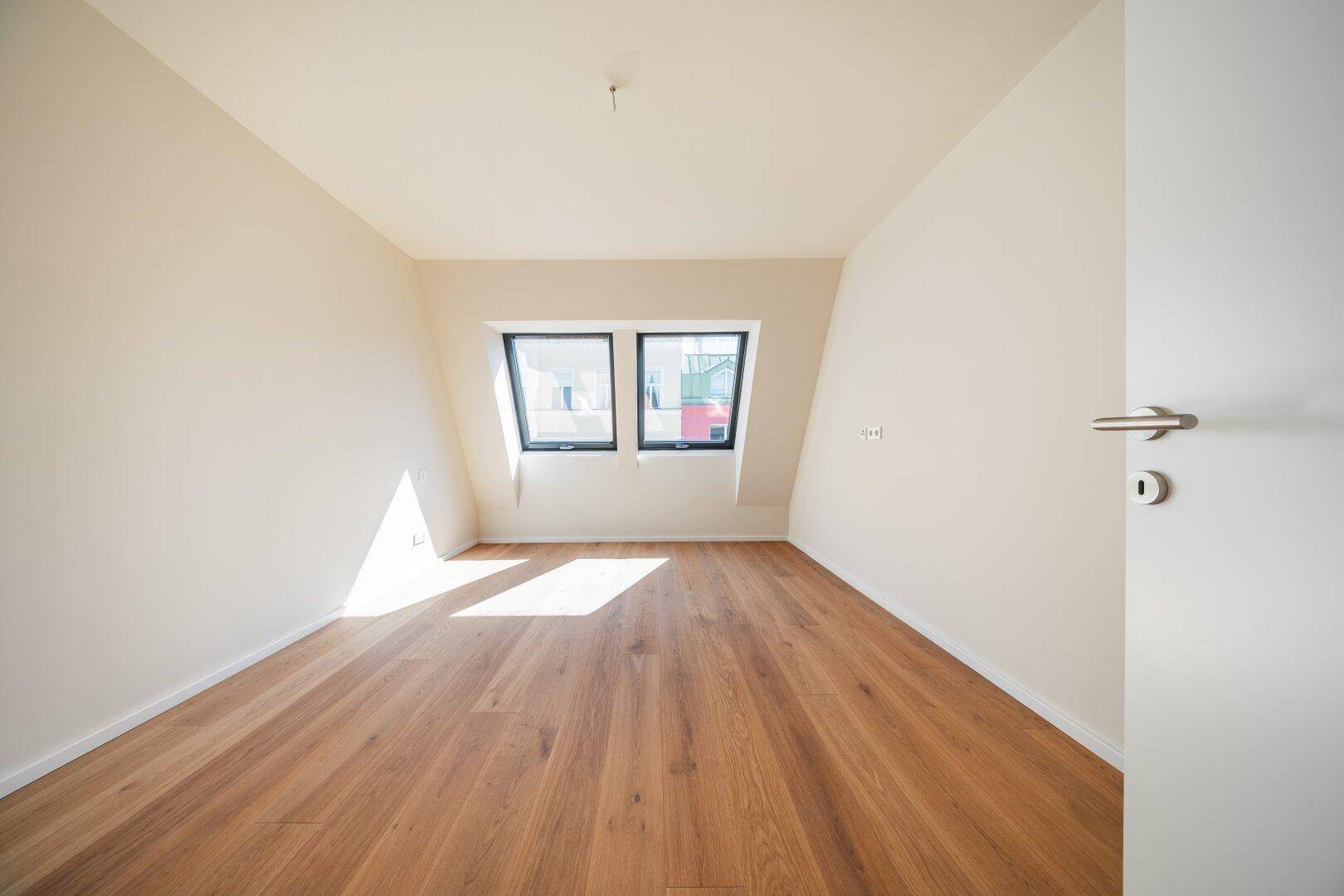 Helles Schlafzimmer mit Holzboden und zwei Dachfenstern, die für eine angenehme Belichtung sorgen.