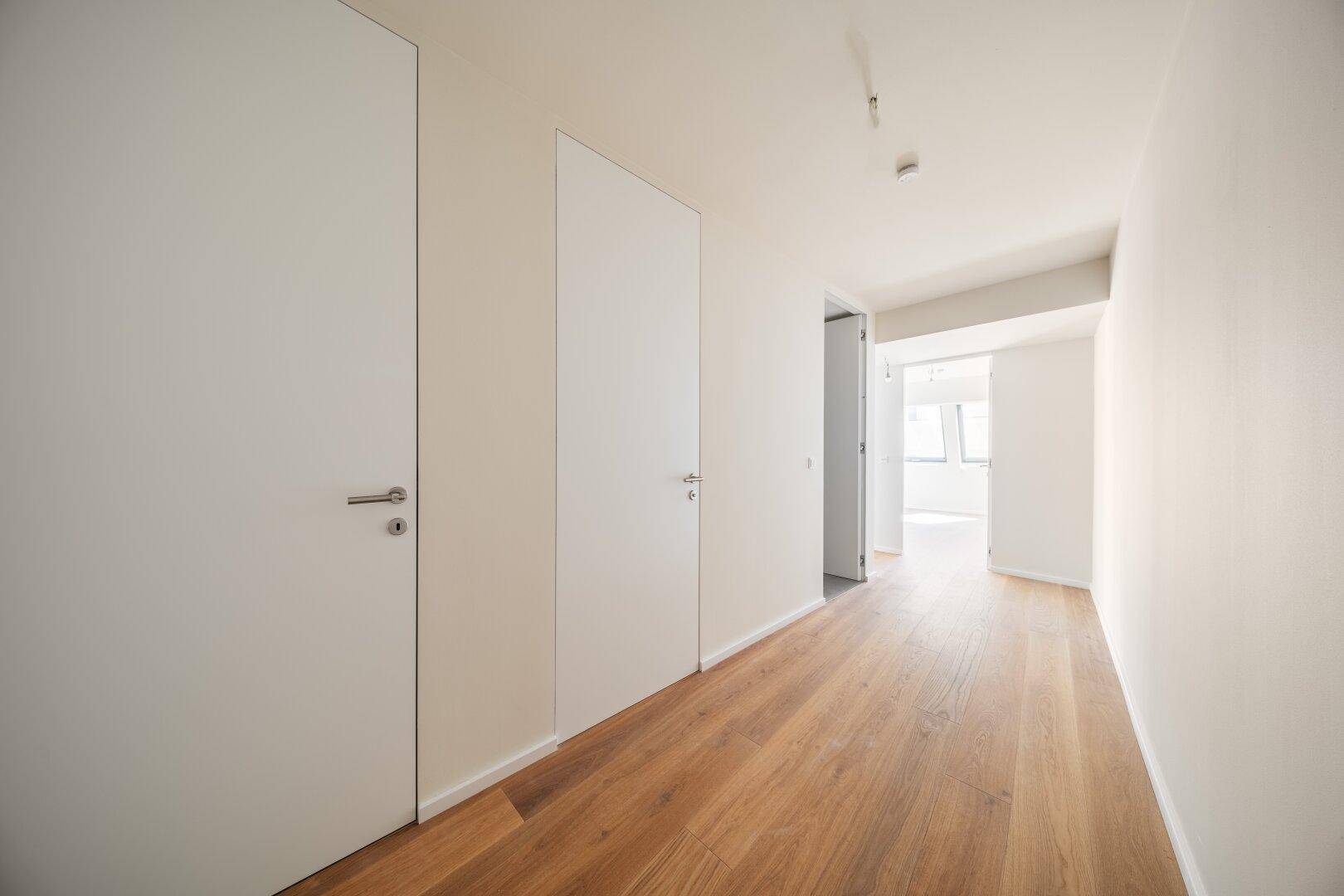 Moderner Flur mit Holzboden und minimalistischen weißen Türen, die in weitere Räume führen.