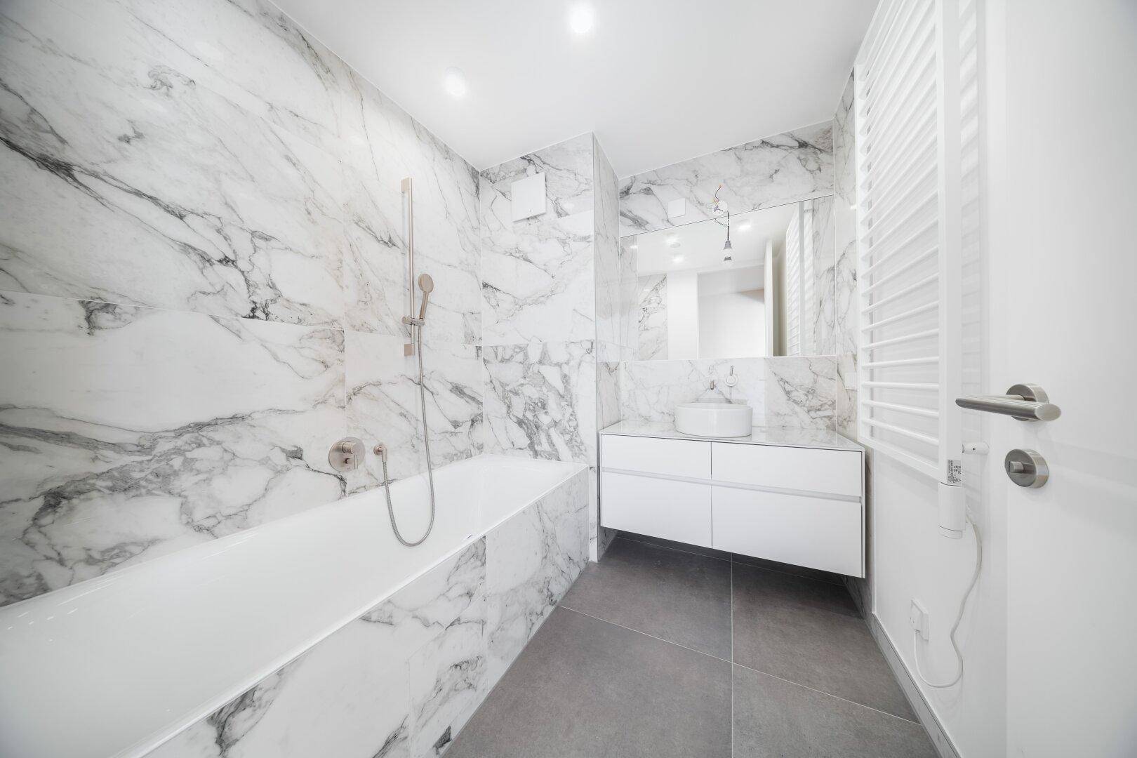Modernes Badezimmer mit Marmorfliesen, Badewanne und elegantem Waschtisch mit Spiegel.