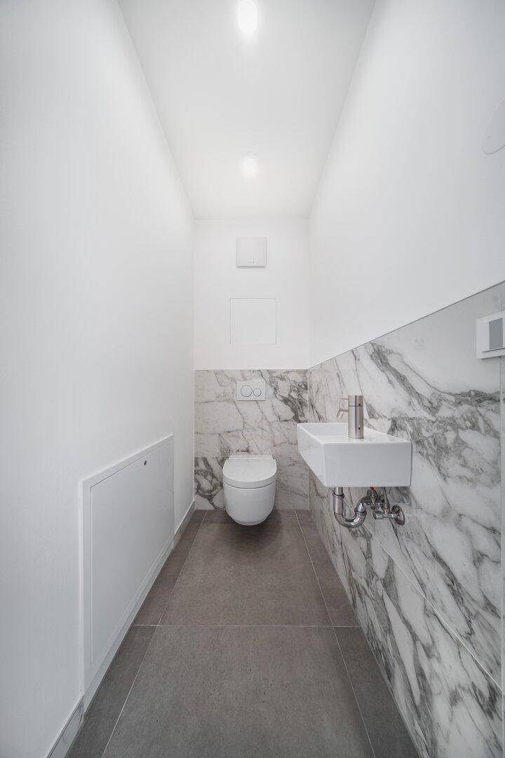 Schmale Gästetoilette mit Marmorwand, wandhängendem WC und modernem Waschbecken.