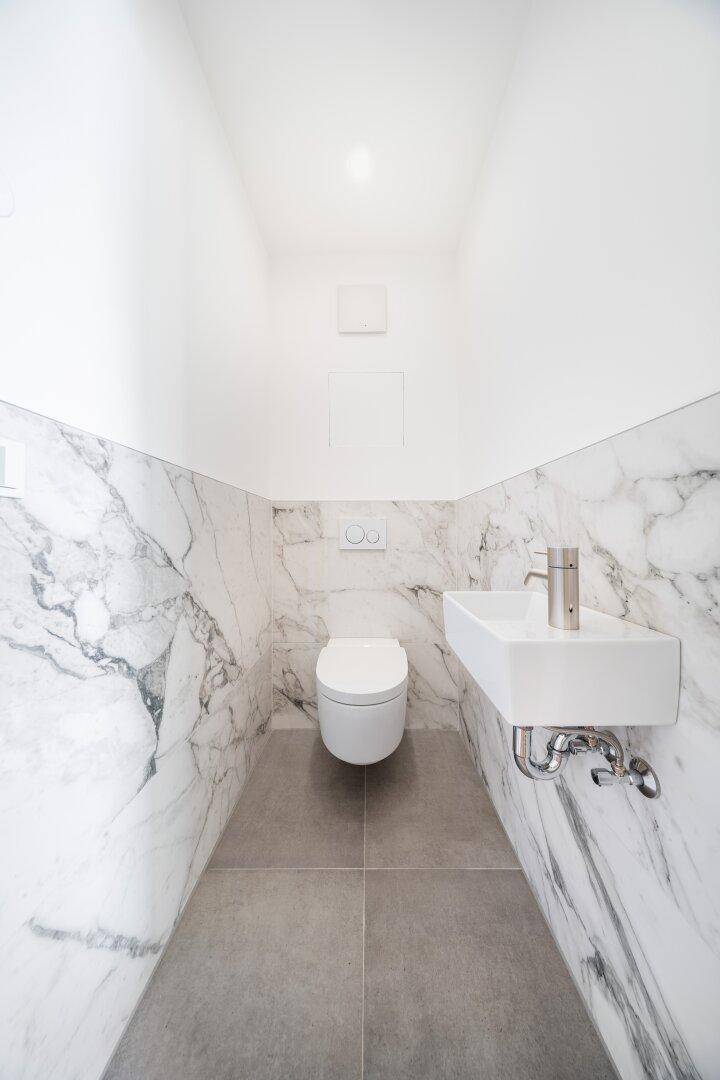 Modernes Gäste-WC mit Marmorfliesen, wandhängender Toilette und kleinem Waschbecken.
