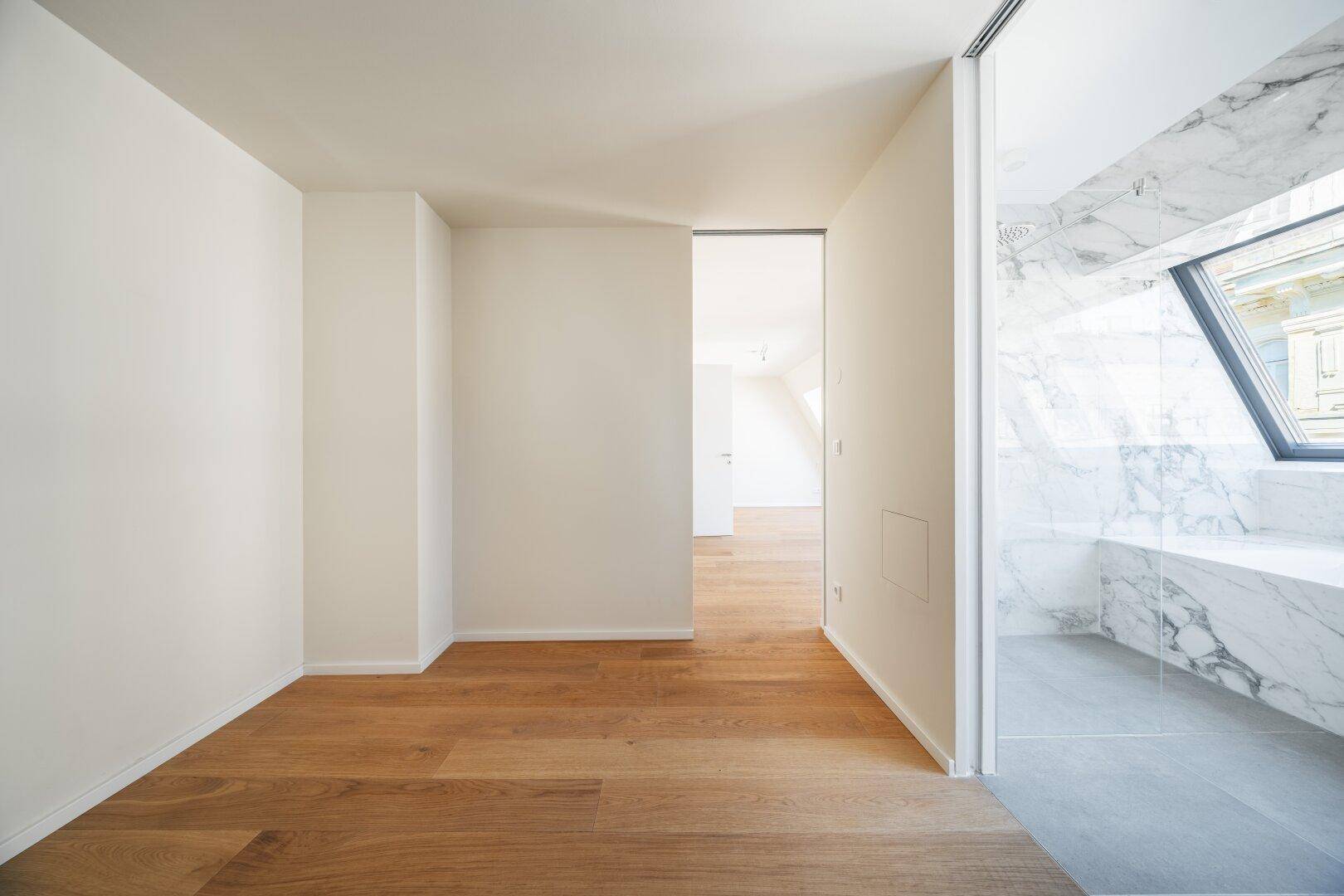 Heller Flur mit Holzboden, der zu einem modernen Badezimmer mit Marmoroberflächen führt.