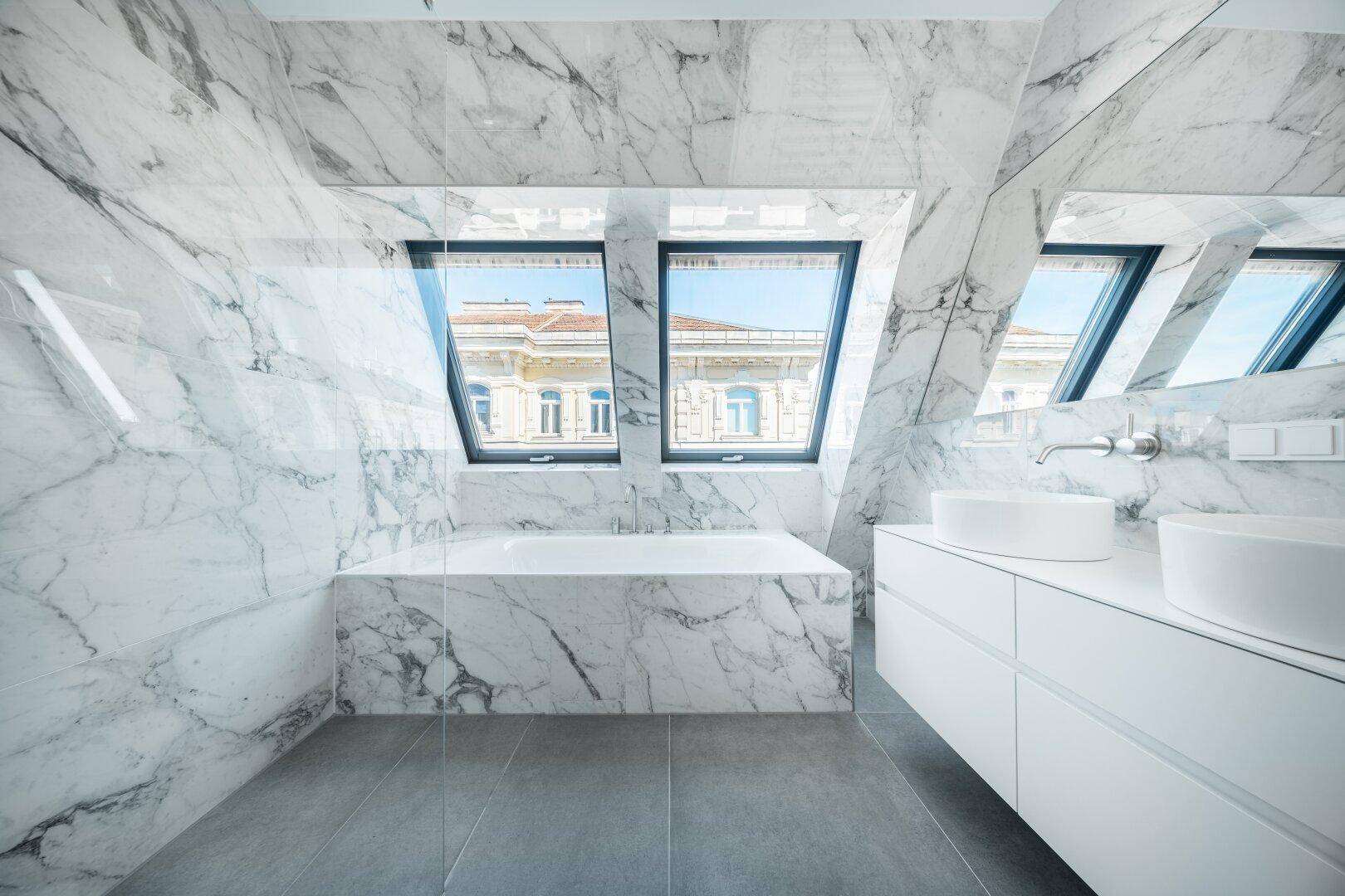 Luxuriöses Badezimmer mit Marmorfliesen, Doppelwaschbecken und Badewanne unter Dachfenstern.