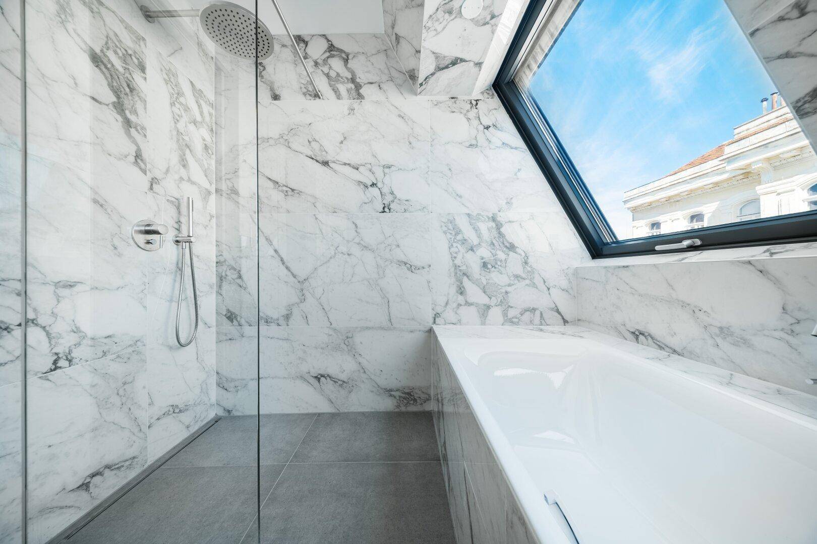 Modernes Badezimmer mit Marmorfliesen, Badewanne, Regendusche und großem Dachfenster.