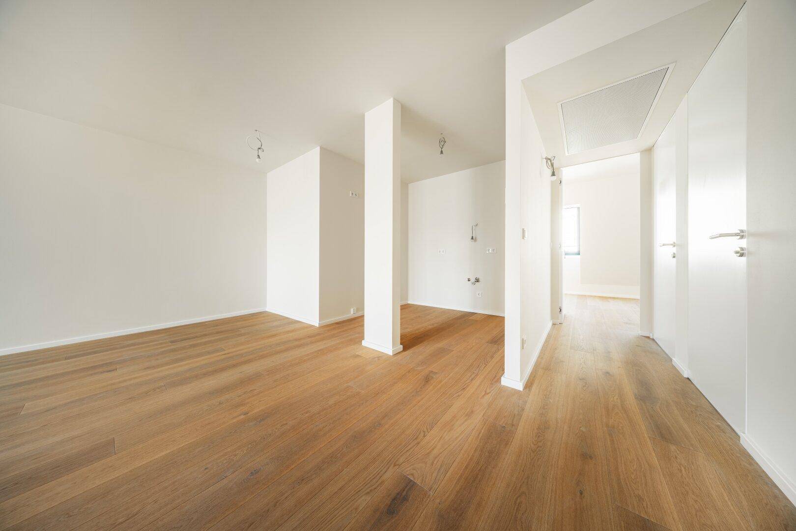 Offener, heller Raum mit Holzboden und Säulen, bietet flexible Gestaltungsmöglichkeiten für Wohnbereiche.