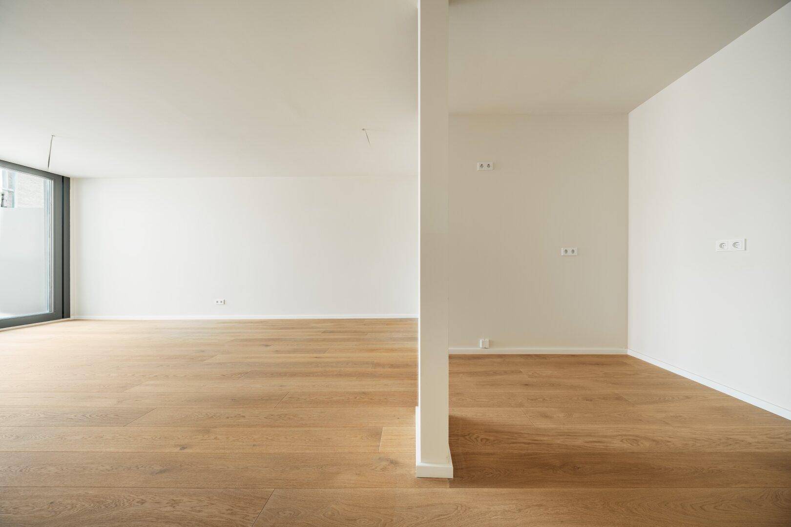 Heller, offener Raum mit Holzboden und Säule, bietet vielseitige Nutzungsmöglichkeiten und Tageslicht.