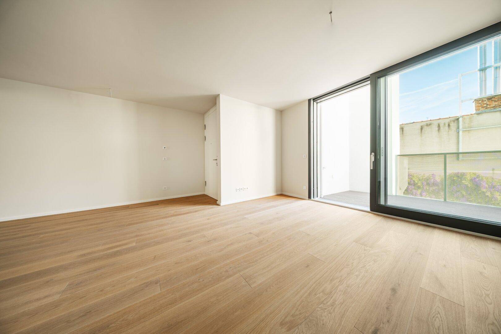 Heller Wohnraum mit Holzboden und großer Schiebetür zum Außenbereich, bietet viel Tageslicht.