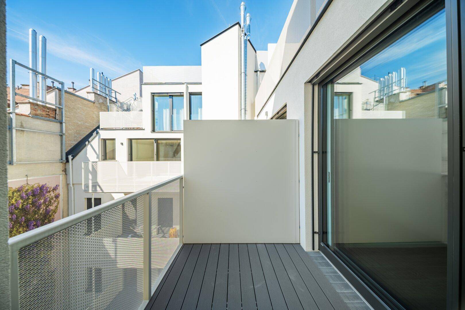Moderner Balkon mit Holzboden und Metallgeländer, bietet einen ruhigen Blick auf den Innenhof.