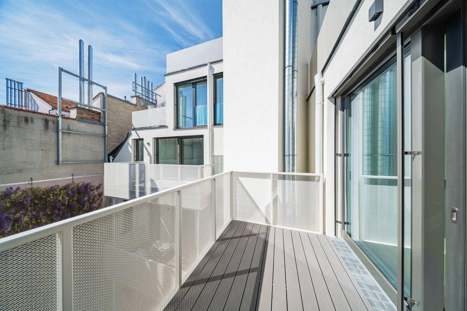 Moderner Balkon mit Holzdielenboden und Metallgeländer, bietet einen Blick auf die umliegenden Gebäude.