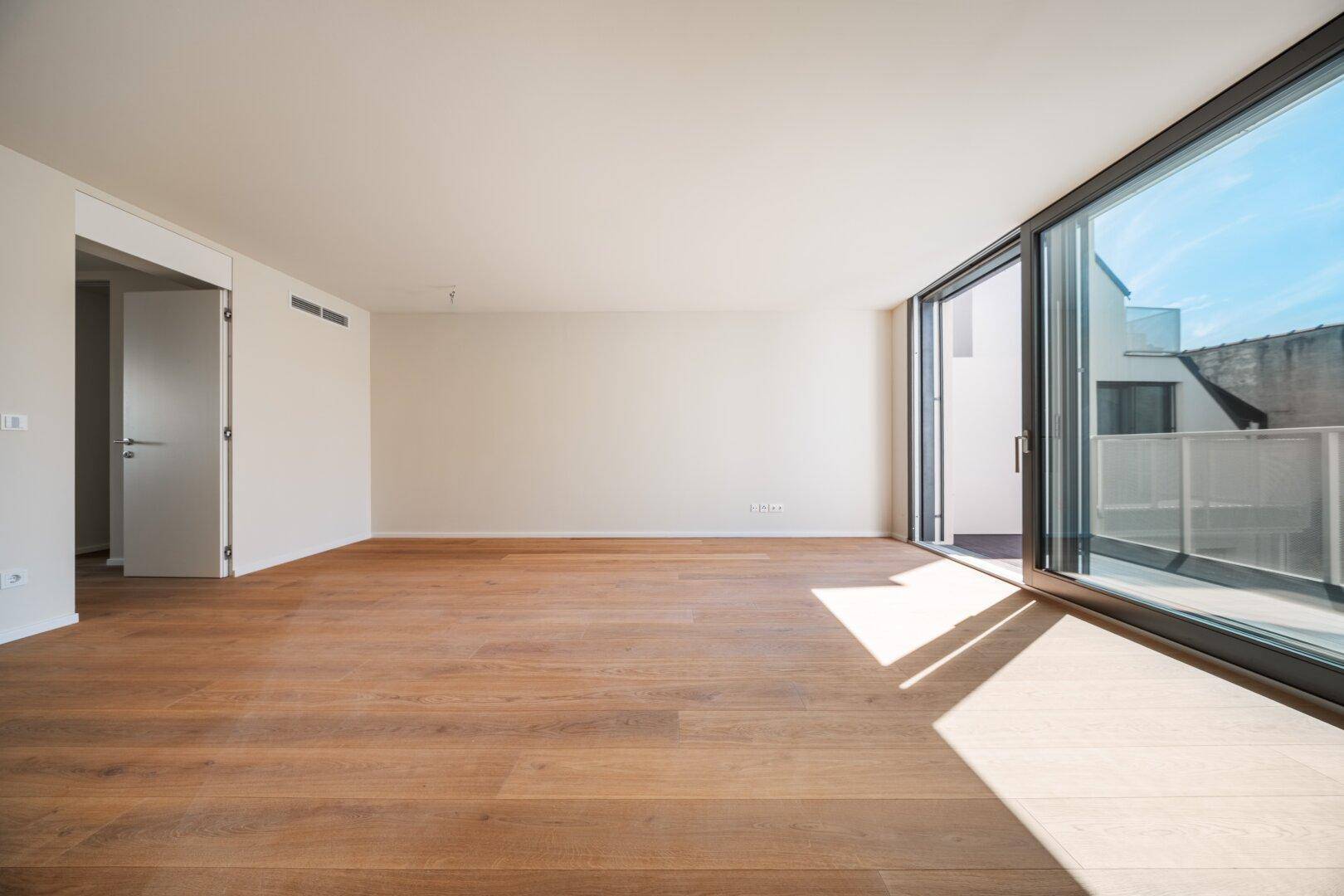 Geräumiges, helles Zimmer mit Holzboden und Zugang zu einem Balkon, bereit zur individuellen Gestaltung.