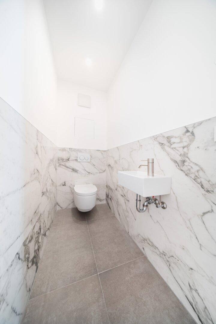 Modernes Gäste-WC mit Marmorfliesen, wandhängender Toilette und kleinem Waschbecken.